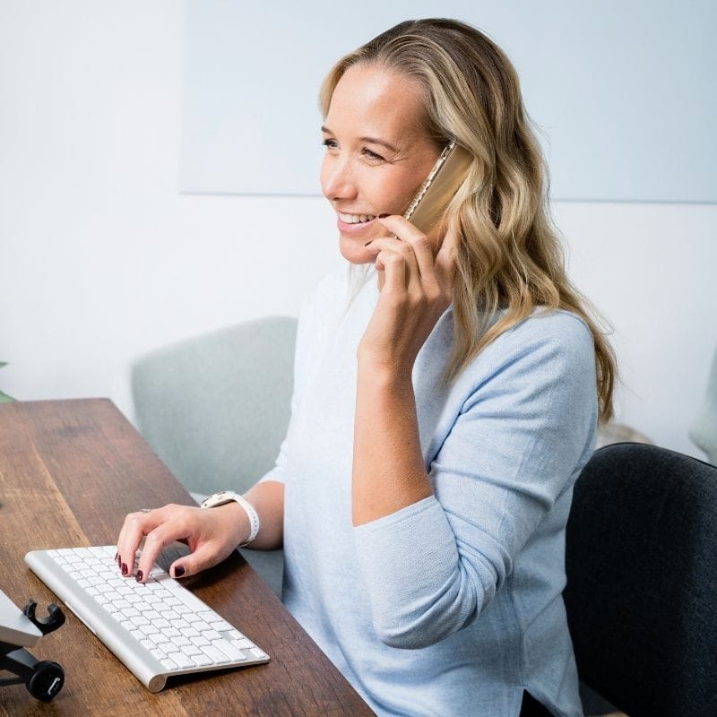 optimiser-discovery-call jessica cairns health coach sitting at desk taking an enquiry call on mobile phone