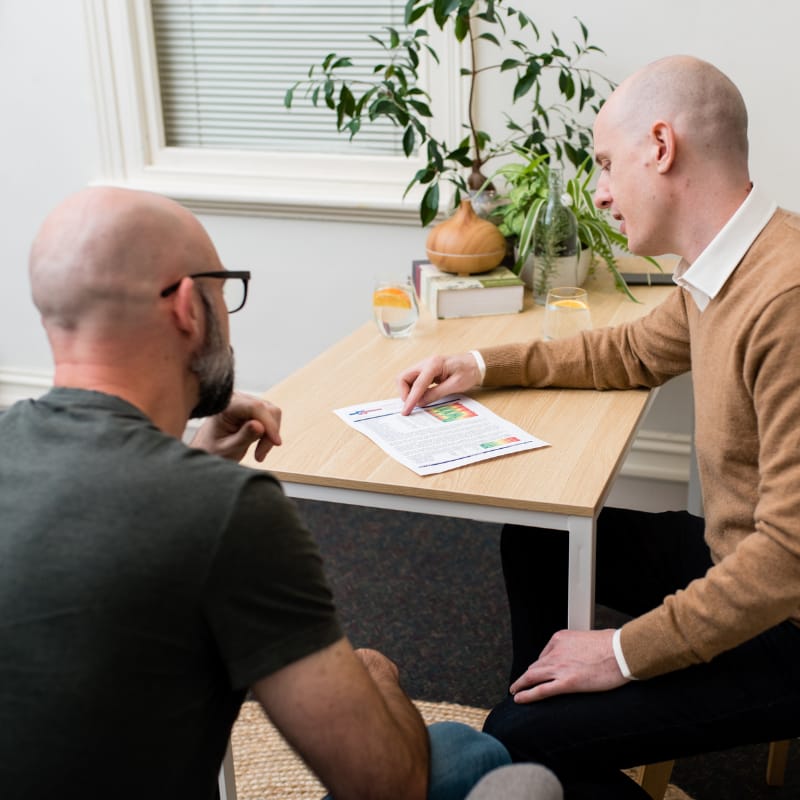 shop-australias-best-blood-test-5 Two people looking over test results in the medical practice of Melbourne Functional Medicine, the space is neutral, modern and clean with a plant and natural health books in the background.