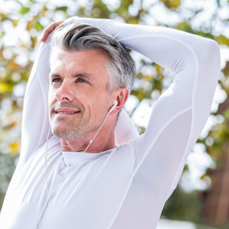 fit middle aged woman in athletic clothes pausing mid coastal run to bend forward and rest hands onto knees