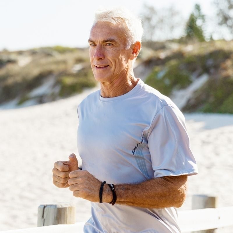 What-is-health-optimisation-hero-1 fit middle aged woman in athletic clothes pausing mid coastal run to bend forward and rest hands onto knees