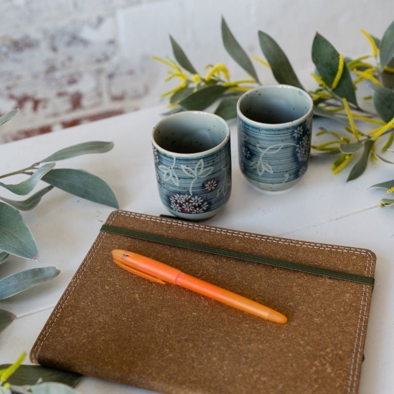 Optimise website images PORTRAIT - 3 notebook with orange pen, tea cups and eucalyptus foliage.