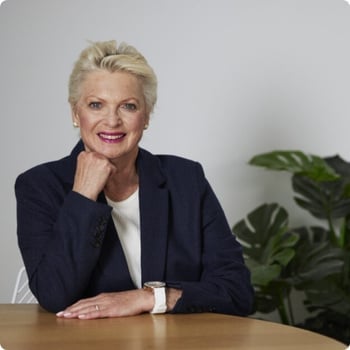 dr-wendy-sweet older woman wearing suit sitting at table elbow resting on table hand on chin
