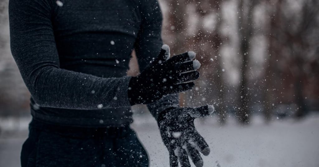 strong-winter-immunity person standing in snow dusting snow off their black gloves