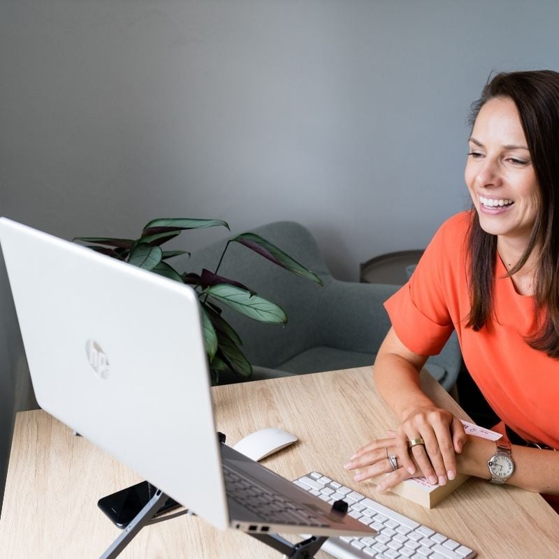 female smiling wearing orange dress on health coaching telehealth via laptop