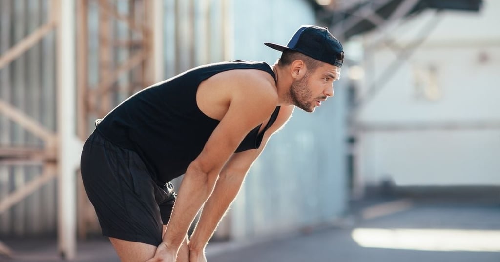 vo2-max man wearing shorts tank top leaning forward hands resting on thighs looking forward