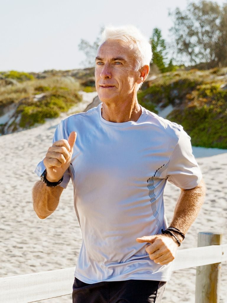 fit middle aged woman in athletic clothes pausing mid coastal run to bend forward and rest hands onto knees